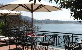 Ein malerischer Blick auf einen ruhigen See, umgeben von Bäumen und einem einladenden Restaurantbereich mit Sonnenschirmen.
