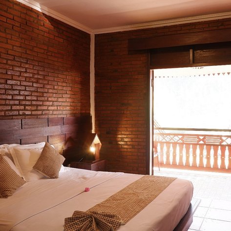 Ein gemütliches Hotelzimmer mit Ziegelwänden, einem großen Bett und einem Balkon, der viel Tageslicht hereinlässt.