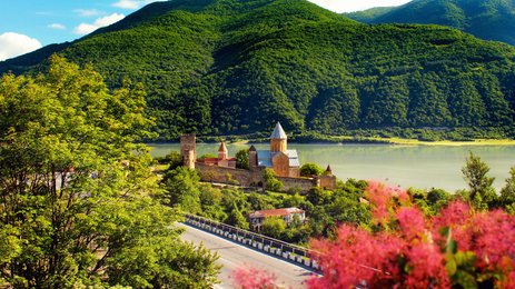 Eine malerische Landschaft mit einem historischen Kloster, umgeben von üppigen grünen Bergen und einem ruhigen See.