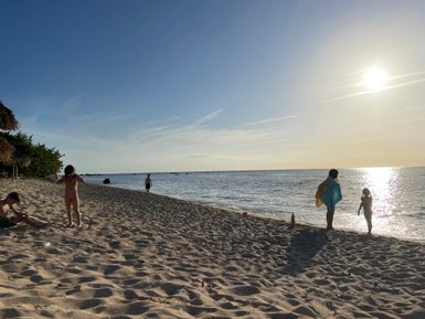 Am Strand spielen Kinder im Sand, während die Sonne über dem ruhigen Wasser untergeht und eine entspannte Atmosphäre schafft.