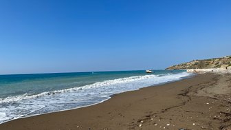 Ein ruhiger Strand mit sanften Wellen, die an den goldenen Sand schlagen, unter einem strahlend blauen Himmel.