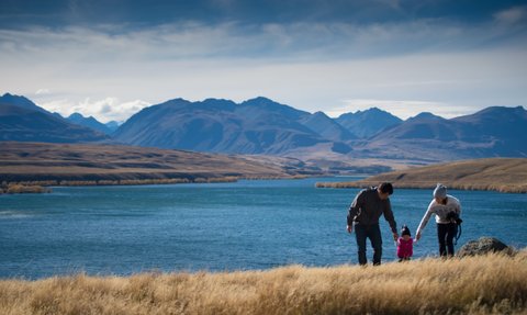 Eine Familie genießt einen sonnigen Tag am Wasser, während die Berge im Hintergrund majestätisch aufragen.