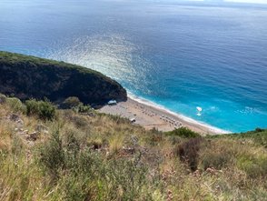 Ein atemberaubender Blick auf den Gjipe Strand, umgeben von grünen Hügeln und glitzerndem, blauem Wasser.