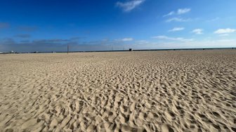 Ein weitläufiger Sandstrand erstreckt sich unter einem klaren blauen Himmel, ideal für einen entspannten Tag am Meer.