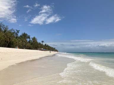 Ein ruhiger Strand mit feinem, weißen Sand erstreckt sich unter einem strahlend blauen Himmel und sanften Wellen.