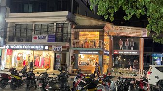 Eine belebte Straße in Pokhara mit verschiedenen Geschäften, darunter 'Women for Women' und 'The North Face'.