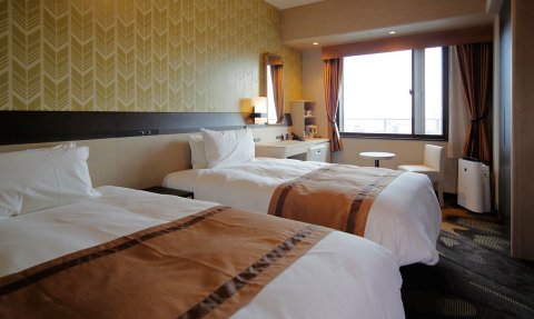 Zwei Einzelbetten mit weißen Bettdecken und braunen Akzenten in einem modernen Hotelzimmer mit Fensterblick.