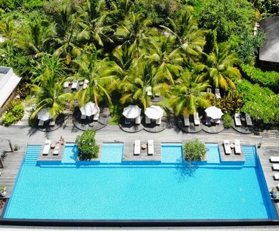 Ein luxuriöser Pool mit klarem Wasser, umgeben von üppigem Grün und stilvollen Liegen unter Sonnenschirmen.