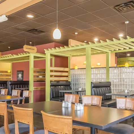 Ein modernes Restaurant mit eleganten Holztischen und bequemen Sitzbänken, die durch grüne Trennwände voneinander abgetrennt sind.