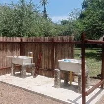 Zwei Waschbecken aus Stein stehen unter einem schattigen Bereich, umgeben von einer natürlichen, grünen Landschaft.