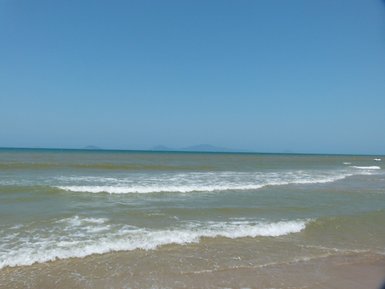 Ein ruhiger Strand mit sanften Wellen, die sanft an den Sandstrand plätschern, unter einem klaren blauen Himmel.