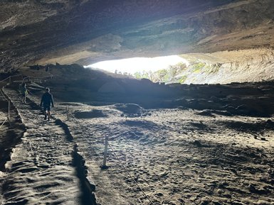 Ein Wanderer geht auf einem schmalen Pfad in einer großen Höhle, die von natürlichem Licht erhellt wird.
