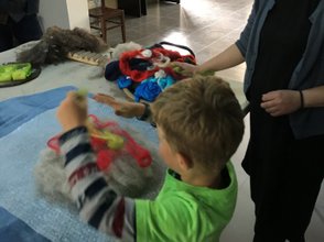Ein Junge in einem grünen T-Shirt arbeitet mit buntem Filzmaterial, während eine Frau ihm dabei zuschaut und lächelt.