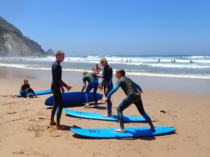 Eine Gruppe von Surfschülern übt auf blauen Surfbrettern am Strand, während die Wellen sanft an den Ufer schlagen.