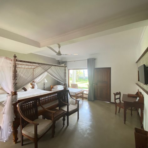 Ein elegantes Zimmer mit einem Himmelbett, umgeben von weißen Vorhängen, und einem Blick auf den Garten durch große Fenster.