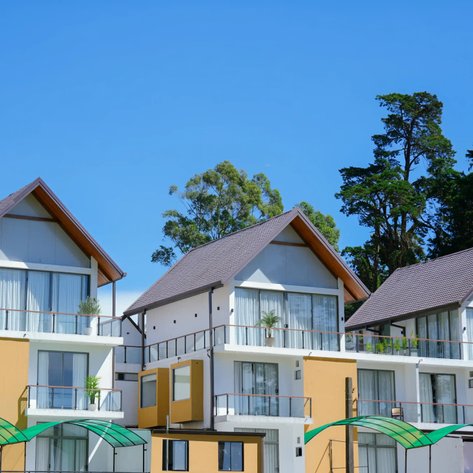 Drei moderne Hotelgebäude mit großen Fenstern und Balkonen, umgeben von üppigem Grün und klarem blauen Himmel.