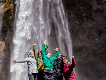 Sechs fröhliche Menschen springen vor dem beeindruckenden Seljalandsfoss-Wasserfall in Island in die Luft.