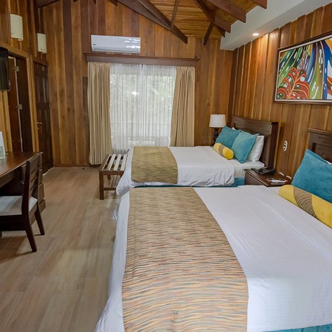 Ein gemütliches Hotelzimmer mit zwei Doppelbetten, Holzverkleidung und buntem Kunstwerk an der Wand.