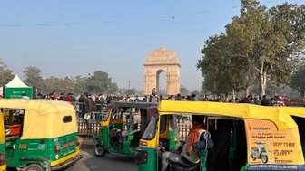 Bunte Tuk-Tuks stehen in der Nähe des India Gate, umgeben von einer Menschenmenge und Bäumen unter klarem Himmel.