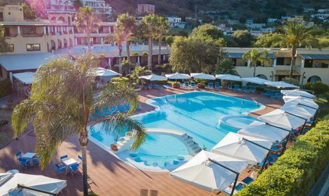 Ein einladender Poolbereich mit Liegen und Sonnenschirmen, umgeben von Palmen und einem Hotel im Hintergrund.