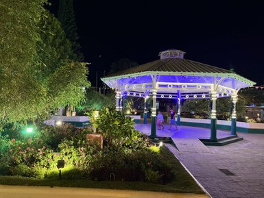 Ein beleuchteter Pavillon in einem Garten voller Blumen, wo Kinder fröhlich umherlaufen und die Nacht genießen.