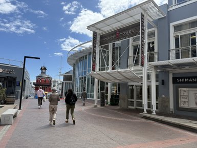 Zwei Personen gehen auf einem gepflasterten Weg in Richtung des Clock Tower Einkaufszentrums in Kapstadt.
