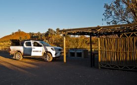 Ein weißes Fahrzeug steht an einem abgelegenen Campingplatz in Namibia, umgeben von sanften Hügeln und Bäumen.