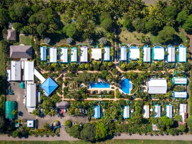 Eine Luftaufnahme eines tropischen Hotels mit blauen Dächern, umgeben von üppigem Grün und einem Pool in der Mitte.