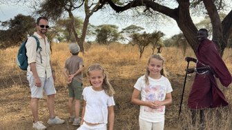 Eine Gruppe von Kindern und einem Erwachsenen posiert fröhlich in der trockenen Savanne, umgeben von hohen Bäumen.