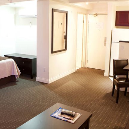 Ein modernes Hotelzimmer mit einem großen Bett, einem Tisch und Stühlen sowie einer kleinen Küchenzeile im Hintergrund.