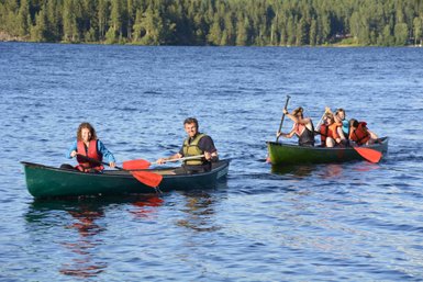 Zwei Kanus gleiten über das ruhige Wasser, während die Paddler fröhlich miteinander interagieren und die Natur genießen.