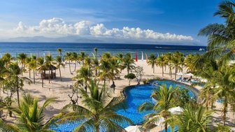 Ein atemberaubender Blick auf einen Pool, umgeben von Palmen und einem weißen Sandstrand unter einem strahlend blauen Himmel.
