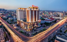 Das Ramada Hotel in Ulaanbaatar erstrahlt in warmem Licht, umgeben von einer lebhaften Stadtlandschaft und fließendem Verkehr.