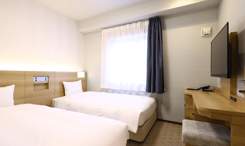 Zwei Einzelbetten in einem modernen Hotelzimmer mit sanften Farben und natürlichem Licht durch das Fenster.