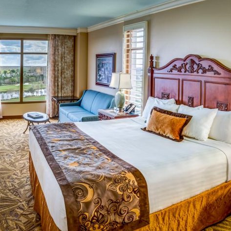 Ein elegantes Hotelzimmer mit einem großen Bett, einem gemütlichen Sofa und Blick auf die Landschaft durch große Fenster.