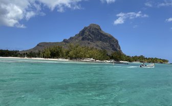 Ein klarer, türkisfarbener Ozean umgibt eine malerische Küste mit üppigen Bäumen und einem beeindruckenden Berg im Hintergrund.