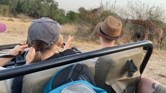 Zwei Kinder beobachten neugierig eine Giraffe aus dem offenen Safari-Jeep im Kruger Nationalpark – Südafrika Reise mit Kindern