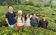 Fünf Personen stehen lächelnd in einer Teeplantage, umgeben von üppigem, grünem Teestrauch.