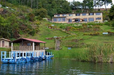 Ein malerisches Hotel am Ufer eines ruhigen Gewässers, umgeben von üppigem Grün und bunten Blumenbeeten.