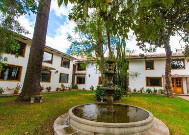 Ein malerischer Innenhof mit einem Brunnen, umgeben von einem gepflegten Garten und modernen Gebäuden im Hintergrund.