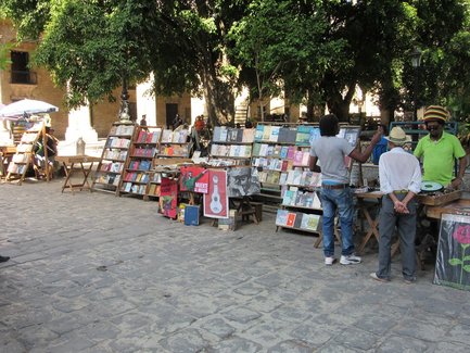 Ein belebter Buchmarkt unter einem großen Baum, wo Verkäufer und Käufer in angeregter Unterhaltung stehen.