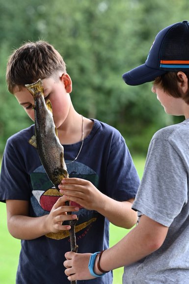 Zwei Jungen stehen im Freien und halten gemeinsam einen frisch gefangenen Fisch, während sie sich konzentriert anschauen.