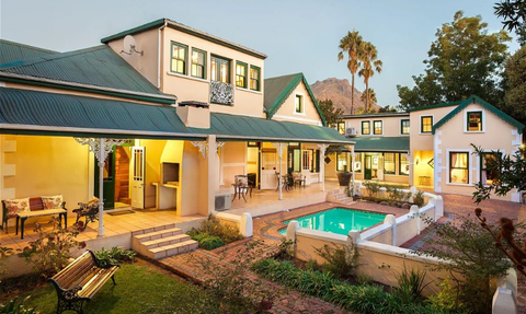 Ein elegantes, zweigeschossiges Haus mit grünem Dach, umgeben von einem gepflegten Garten und einem einladenden Pool.