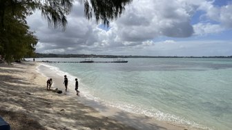 Drei Kinder spielen am Strand, während sanfte Wellen an die Küste schlagen und die Wolken am Himmel vorbeiziehen.