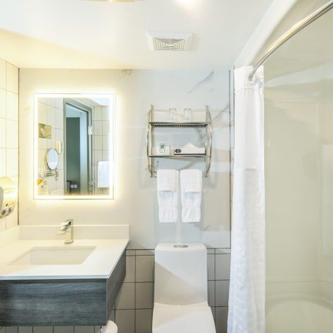 Ein modernes Badezimmer mit einem eleganten Waschbecken, einem beleuchteten Spiegel und weißen Handtüchern auf einem Regal.