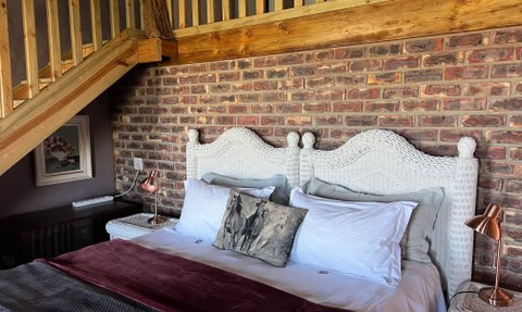 Ein gemütliches Schlafzimmer mit einem großen Bett, umgeben von einer Ziegelwand und Holzdetails, strahlt Ruhe aus.