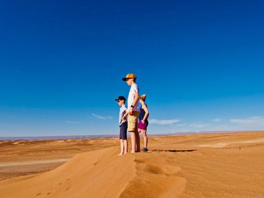 Kinder genießen die Aussicht von einer Dünenkuppe in der Wüste – Familienurlaub in Marokko