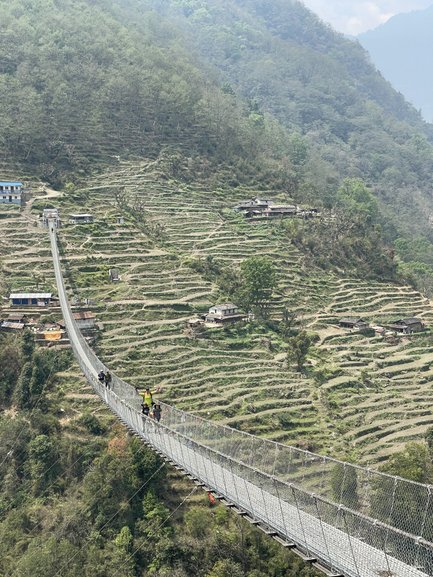 Eine schmale Hängebrücke verbindet zwei Hänge, während Wanderer vorsichtig über die Brücke gehen und die Landschaft genießen.
