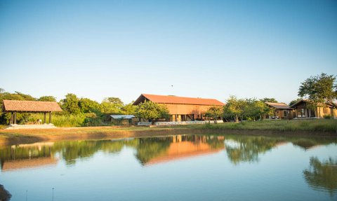 Ein ruhiger Blick auf eine Villa in Sri Lanka, umgeben von üppigem Grün und einem glitzernden Teich im Vordergrund.