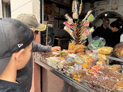 Zwei Jungen betrachten neugierig eine bunte Auswahl an Süßigkeiten und Snacks an einem Marktstand.